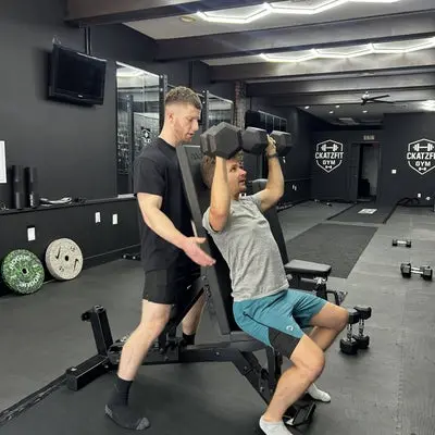 A CKatzFit coach guiding an athlete through a dumbbell press